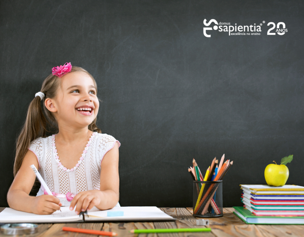 Uma garotinha sentada em uma mesa com lápis e um quadro-negro.