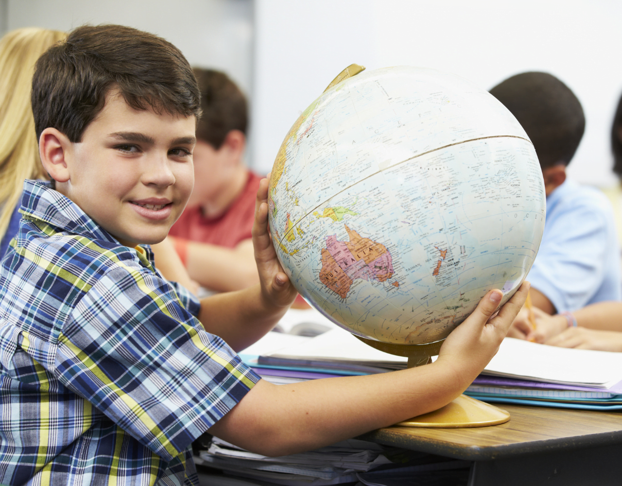 Um menino segurando um globo em frente a uma sala de aula.