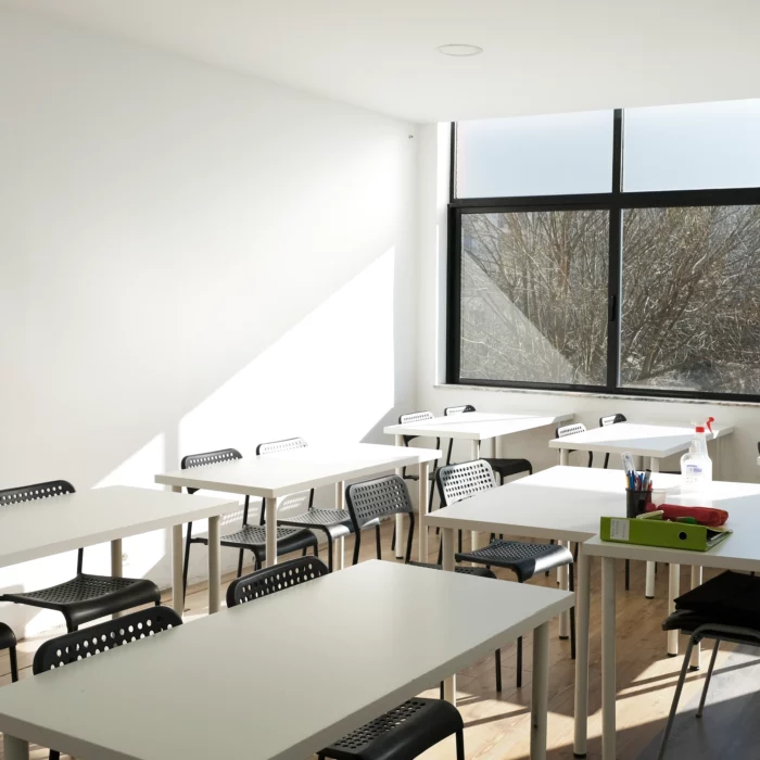 Uma sala de aula com mesas e cadeiras em frente a uma janela.