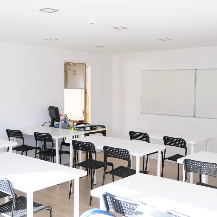 Sala de aula com cadeiras e quadro branco.