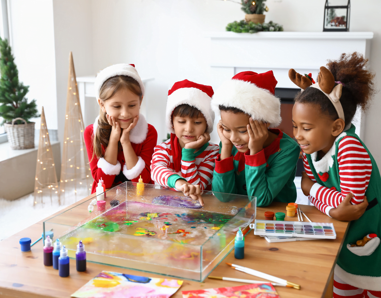 Crianças com chapéus de Papai Noel pintando uma árvore de Natal.