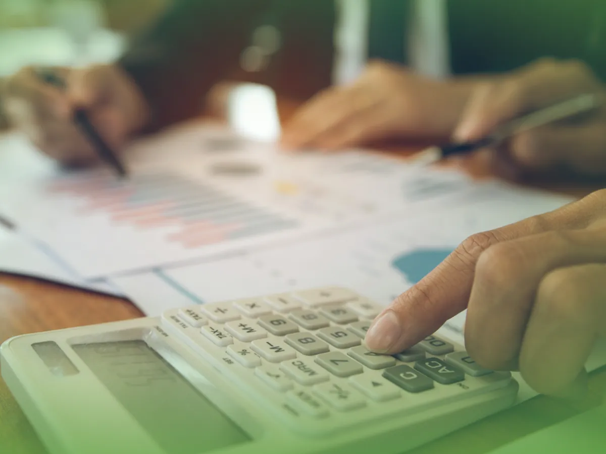 Close de mãos usando Explicações de Cálculo UN. Pacote de Horas e redação de notas sobre documentos financeiros, sugerindo cenário de análise ou planejamento orçamentário.