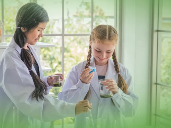 Duas jovens cientistas com batas de laboratório a realizar experiências com Explicações de Ciências Naturais 6.º Ano. Pacote de Horas em béqueres, sorrindo, em laboratório bem iluminado.