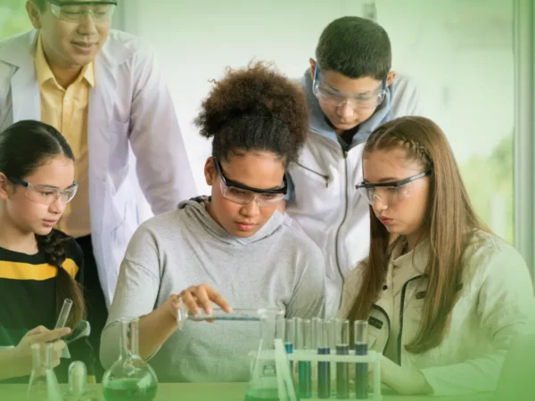 Grupo diversificado de estudantes que realizam uma experiência científica em laboratório, vertendo líquidos em tubos de ensaio, sob a supervisão de um Professor de Explicações de Ciências Naturais 9.º Ano . Instrutor do Pacote de Horas.