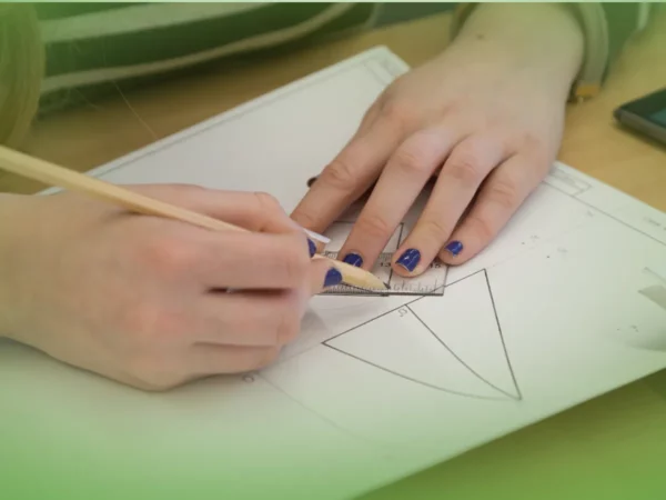 Uma pessoa medindo um triângulo num papel com Explicações de Desenho A 10.º Ano. Pacote de Horas, com foco na tarefa em questão.
