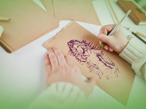 Uma pessoa desenha uma mulher de cabelos compridos em papel pardo, usando Explicações de Desenho A 11.º Ano. Pacote de Horas. Outros papéis e ferramentas de desenho estão espalhados sobre a mesa.