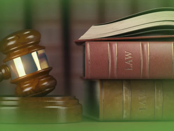 O martelo de um juiz está ao lado de uma pilha de três livros de direito sobre uma mesa, com as palavras "Explicações de Direito 12.º Ano. Pacote de Horas" visíveis nas lombadas de dois livros.