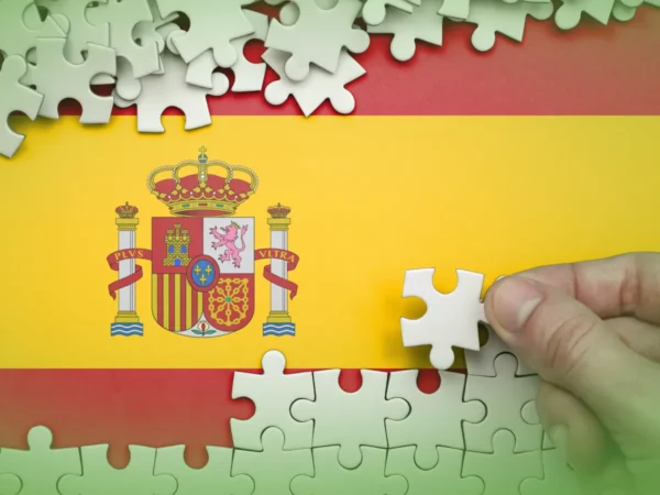 Uma mão coloca uma peça de um quebra-cabeça incompleto com Explicações de Espanhol 11.º Ano. Pacote de Horas com seu brasão nacional.