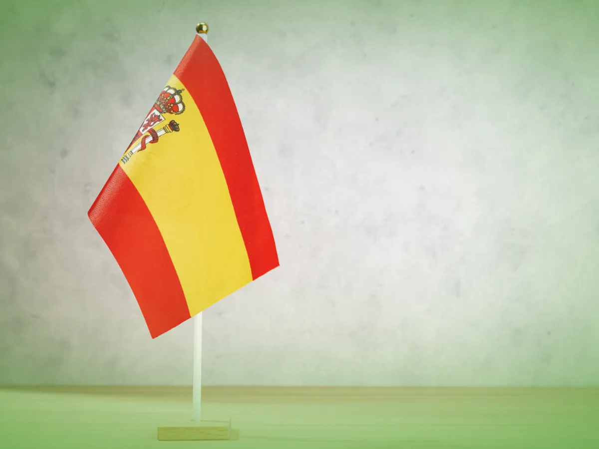 Uma pequena Explicações de Espanhol 7.º Ano . A bandeira do Pacote de Horas está apoiada em uma base de madeira sobre um fundo verde claro texturizado.