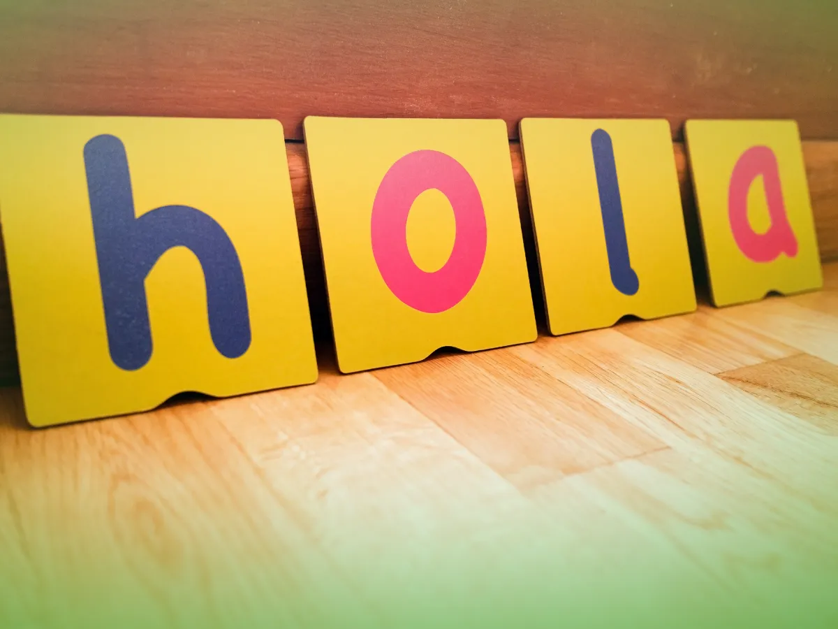 Quatro Explicações de Espanhol 8.º Ano . Cartões Pacote de Horas com letras escritas "hola" ficam enfileirados contra um fundo de madeira.