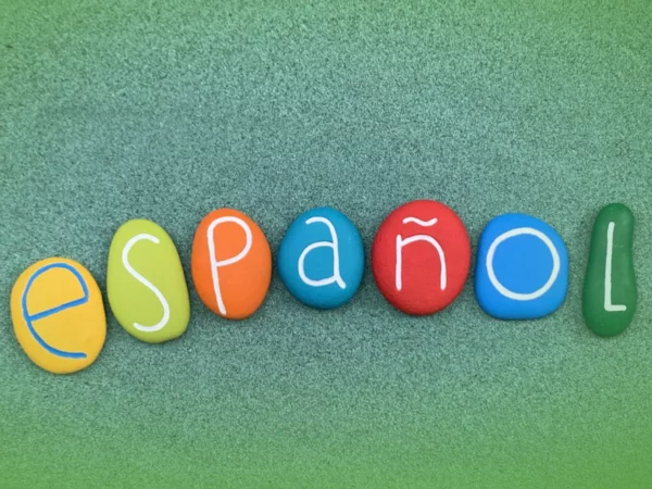 Pedras coloridas com a grafia "Explicações de Espanhol 9.º Ano . Pacote de Horas" sobre fundo de feltro verde, cada pedra pintada em uma cor brilhante diferente com letras em tons contrastantes.