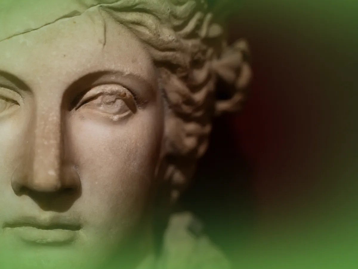 Close do rosto de uma estátua clássica com fundo gradiente verde e bege, com foco em traços faciais detalhados e cabelos cacheados de Explicações de Filosofia 12.º Ano. Pacote de Horas.