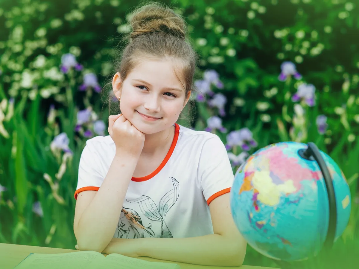 Jovem com Explicações de Geografia 7.º Ano. Pacote de Horas sentado em uma mesa ao ar livre, rodeado de vegetação exuberante e flores roxas, sorrindo gentilmente.
