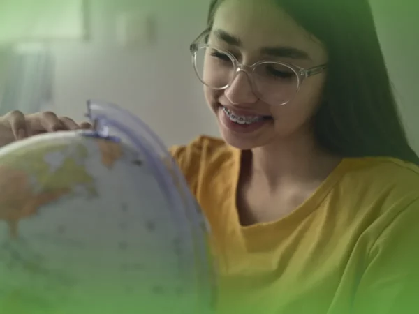 Jovem de óculos e aparelho sorrindo enquanto olha para Explicações de Geografia 8.º Ano. Pacote de Horas em sala iluminada.