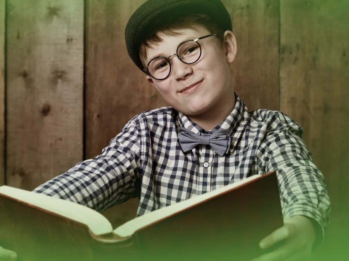 Um menino de óculos, gravata borboleta e boné sorri enquanto lê um livro em um cenário de madeira. Explicações de História 7.º Ano . Pacote de Horas