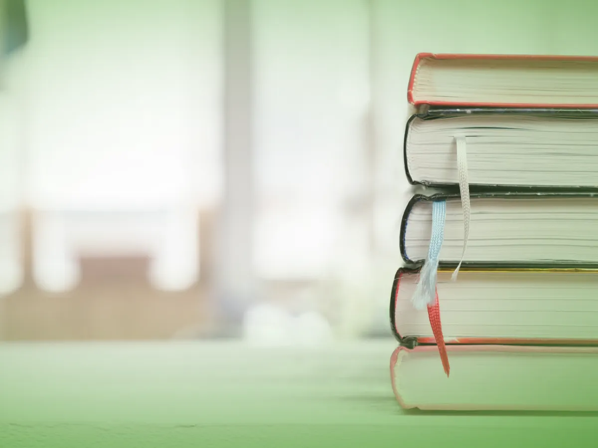 Uma pilha de quatro Explicações de História 8.º Ano . Pacote de Horas, com marcadores, colocados sobre superfície verde sobre fundo desfocado.