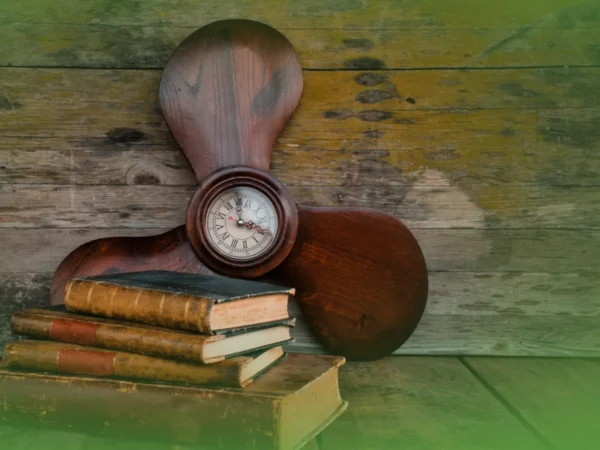 Uma bússola vintage apoiada em livros antigos com uma hélice de madeira ao fundo, colocada contra uma parede verde e de madeira. "Explicações de História 9.º Ano. Pacote de Horas