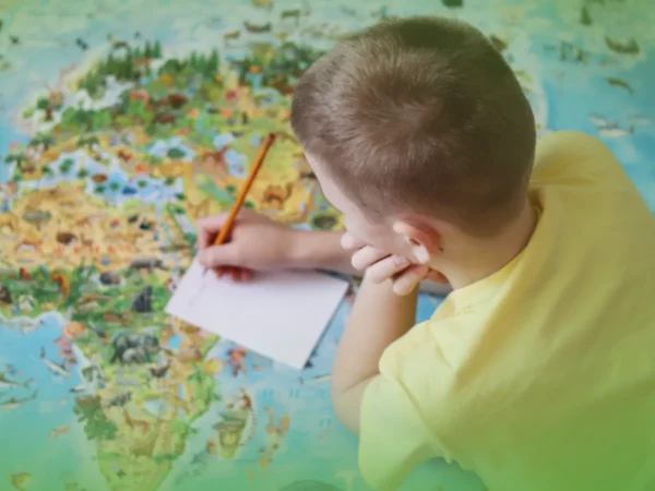 Rapaz de camisa amarela a escrever num papel ao lado de Explicações de História e Geografia de Portugal 6.º Ano . Mapa de quebra-cabeça do Pacote de Horas.