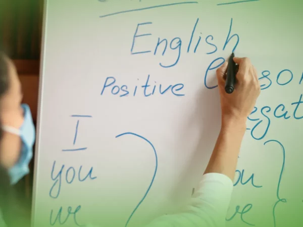 Pessoa mascarada escrevendo Explicações de Inglês 5.º Ano . Pacote de Horas em quadro branco com marcador.