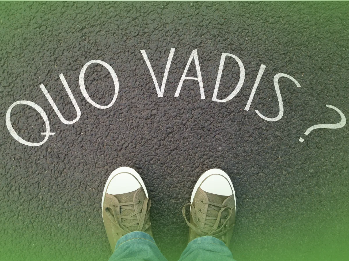 Pessoa em pé no passeio com as Explicações de Latim A 10.º Ano. Pacote de Horas pintado de branco, visto de cima, mostrando apenas os pés calçando tênis.