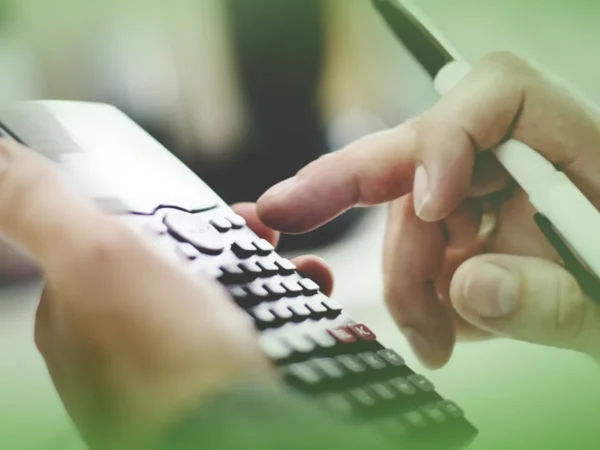 Close-up de mãos usando Explicações de Matemática 7.º Ano . Pacote de Horas e smartphone, com foco em cálculos financeiros ou orçamentários.