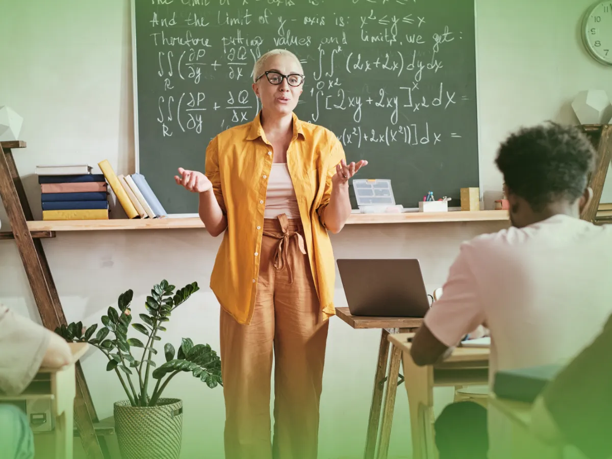 Um professor está em frente a uma sala de aula, explicando uma equação matemática complexa num quadro negro a um aluno sentado numa secretária com Explicações de Matemática B 12.º Ano - Pacote de Horas.