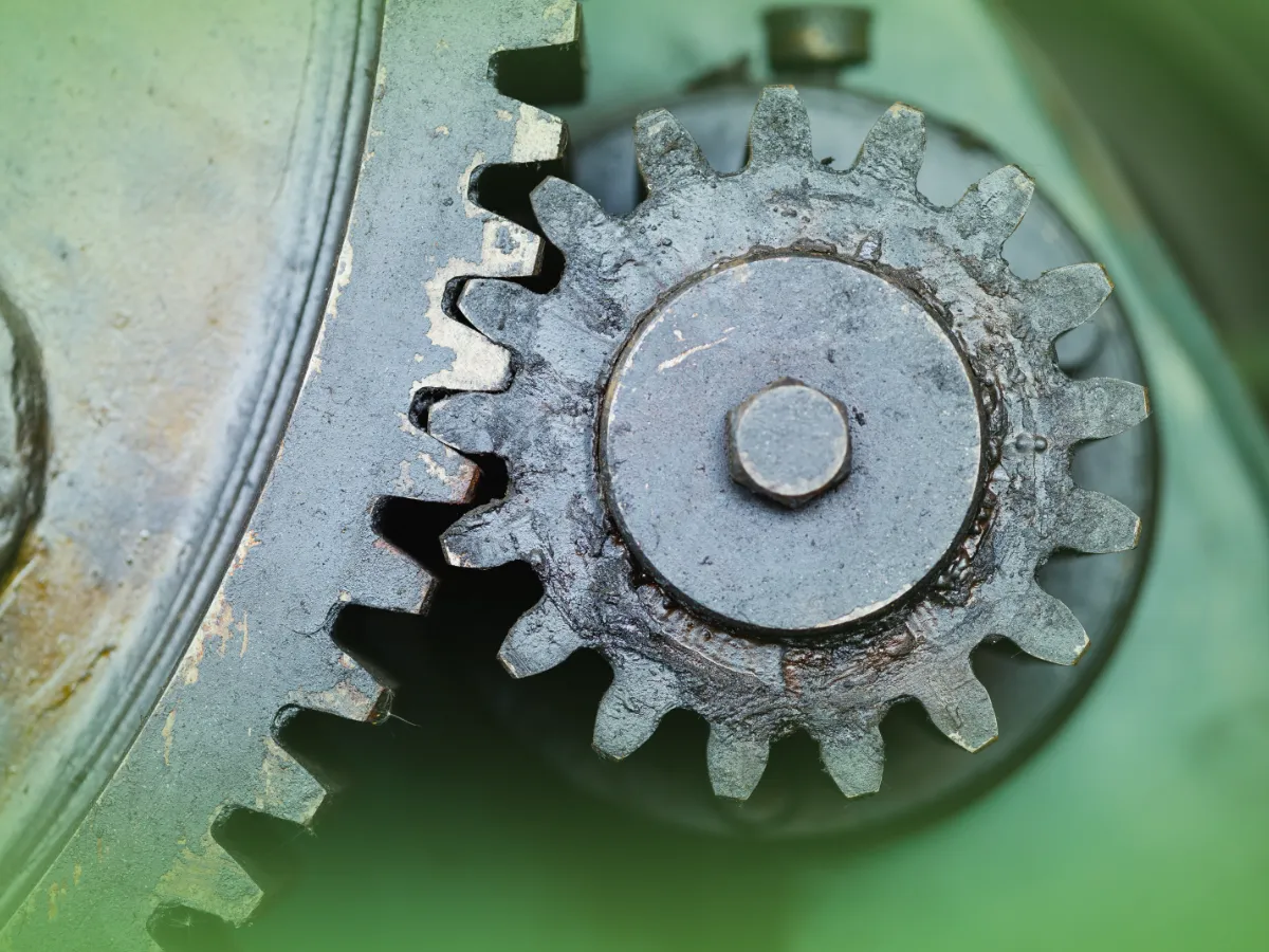 Close de uma engrenagem metálica enferrujada com dentes intrincados, montada em uma máquina com fundo verde desfocado Explicações Mecânica dos Sólidos. Pacote de horas.