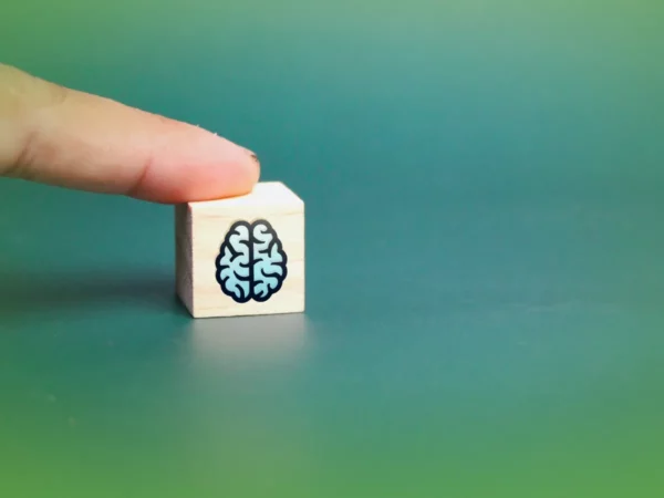 Um dedo toca um bloco de madeira com um ícone de cérebro sobre fundo verde, Explicações de Psicologia 12.º Ano. Pacote de Horas.