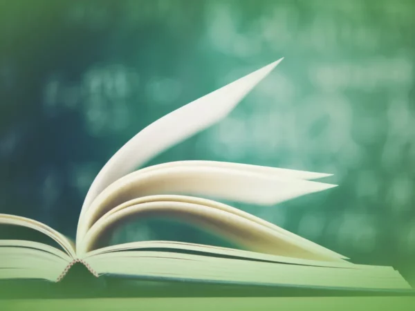 Abra Explicações de Sintaxe UN . Pacote de Horas sobre uma mesa com páginas tremulando, fundo verde desfocado sugerindo um ambiente tranquilo, possivelmente ao ar livre.