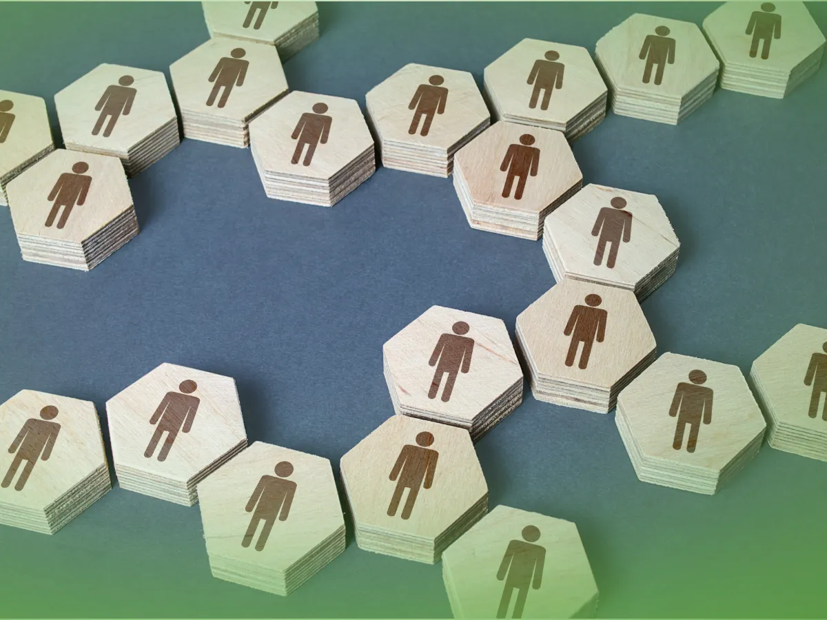 Ladrilhos de madeira hexagonais com silhuetas humanas em vários tons de castanho dispostos num padrão sobre uma superfície verde. Explicações de Teoria da Comunicação ONU. Pacote de Horas