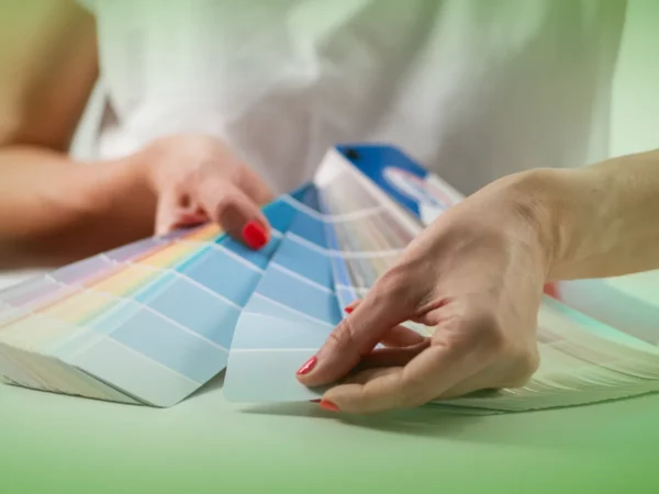 Uma pessoa com esmalte vermelho selecionando uma amostra de cor de Explicações de Teorias do Design UN. Pacote de Horas espalhado sobre uma mesa.