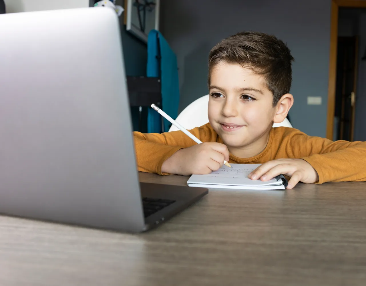Um menino sentado em uma mesa com um laptop e uma caneta.