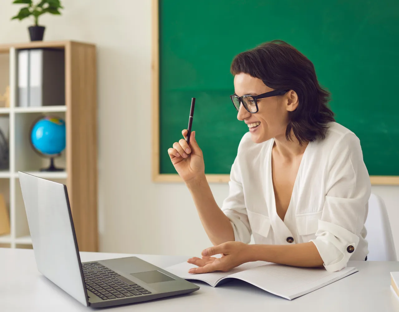 Uma mulher de óculos está sentada em uma mesa com um laptop à sua frente.