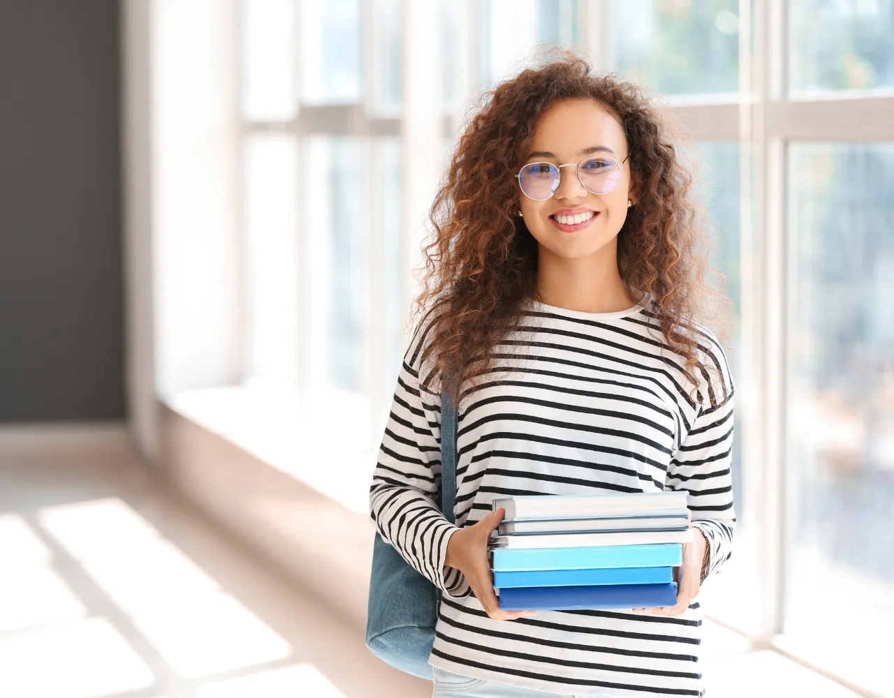 Uma jovem segurando uma pilha de livros de várias disciplinas escolares.