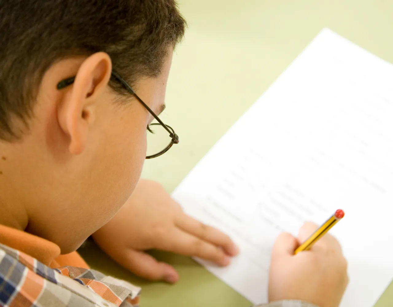 Um menino está escrevendo no papel com um lápis.