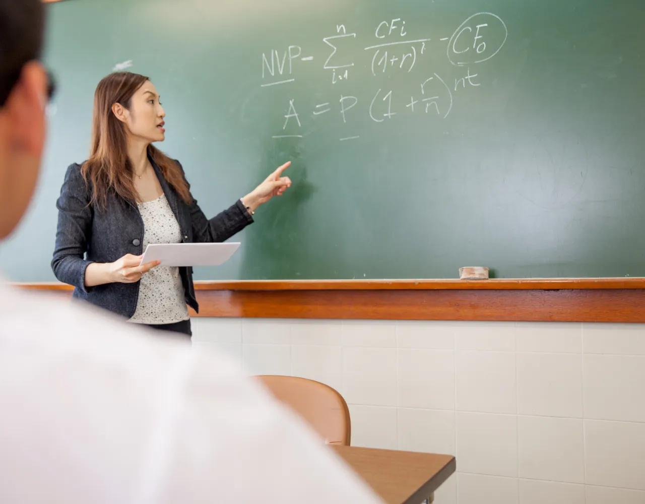 Uma mulher está dando uma aula em frente a um quadro negro.