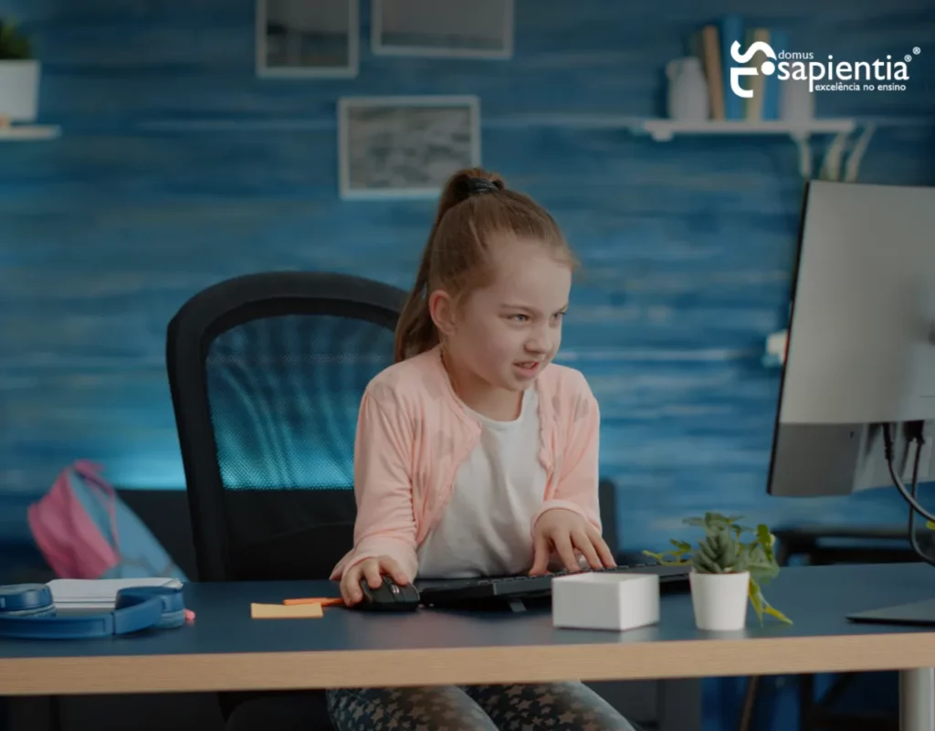 Uma jovem com rabo de cavalo e jaqueta rosa usa um computador em uma sala de aula com uma parede de madeira azul ao fundo.