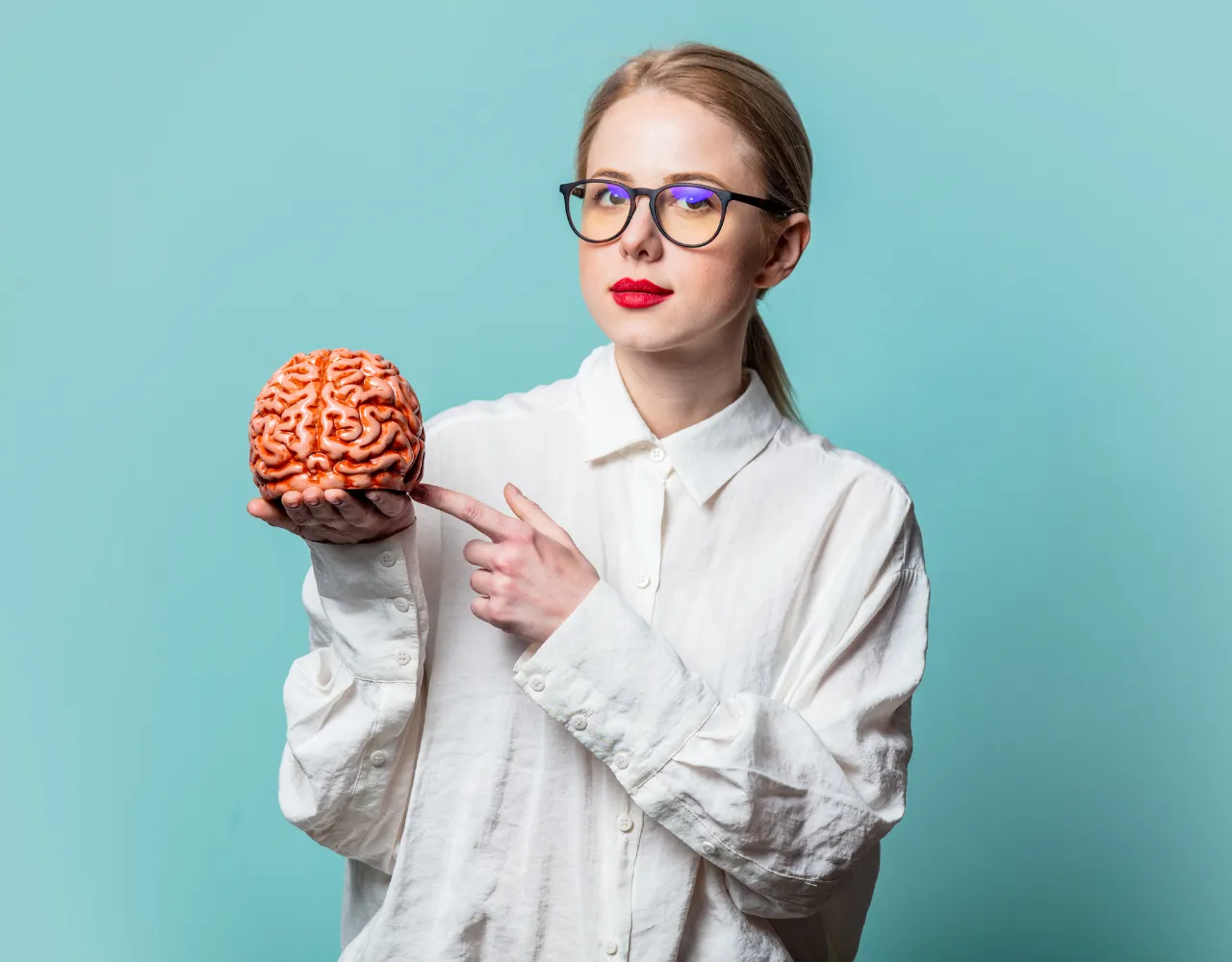 Mulher de óculos segurando um modelo de cérebro e apontando para ele.
