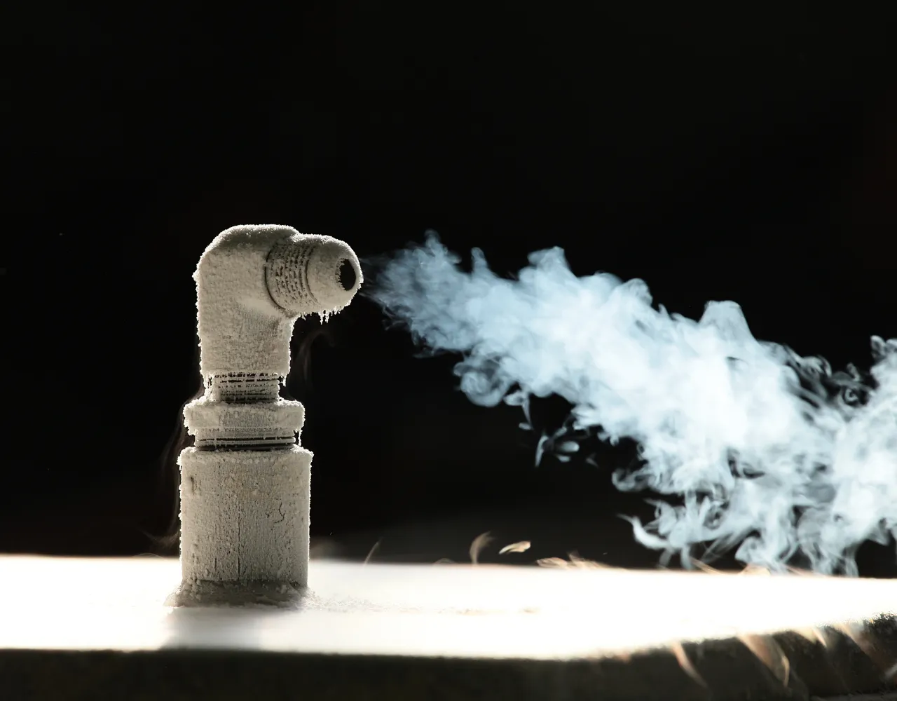 Um cachimbo com articulação em cotovelo emite uma nuvem de fumaça branca ou vapor contra um fundo escuro.