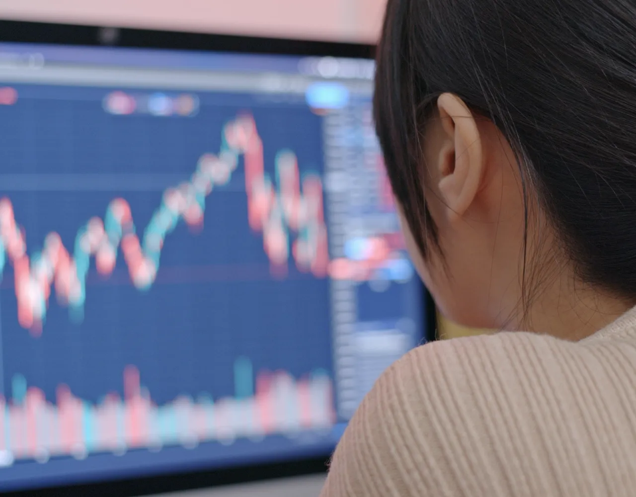 Uma pessoa olha para a tela de um computador que exibe um gráfico financeiro flutuante com vários pontos de dados e gráficos.