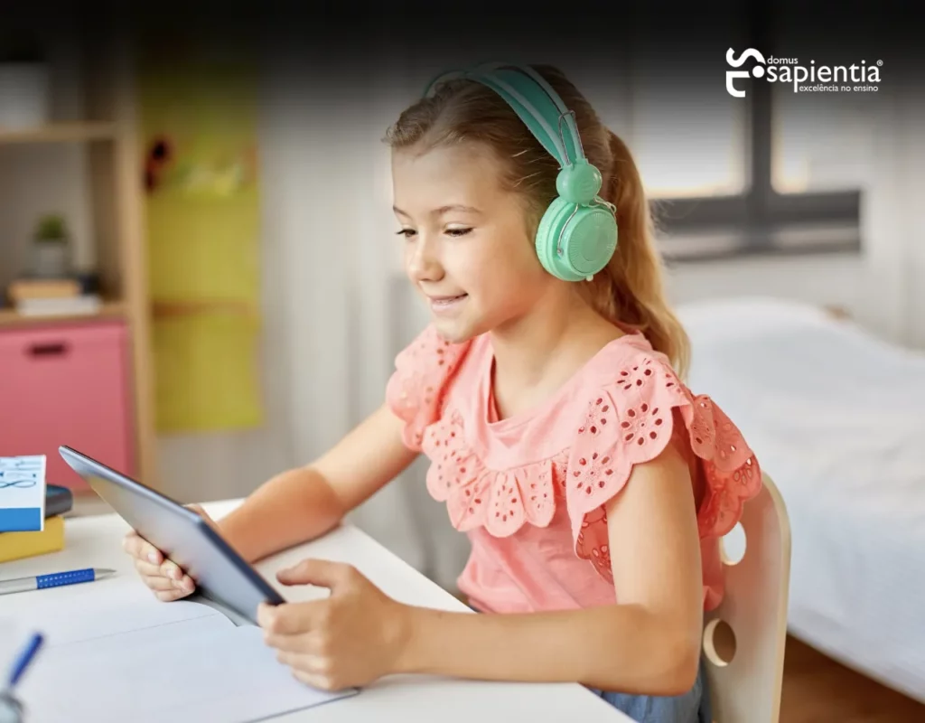 Uma jovem usando fones de ouvido verdes está sentada em uma mesa, sorrindo para um tablet em uma sala bem iluminada.